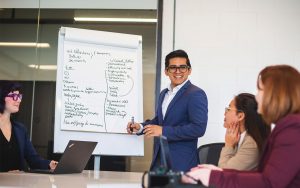 A man standing in front of a research group, with notes on a board behind him