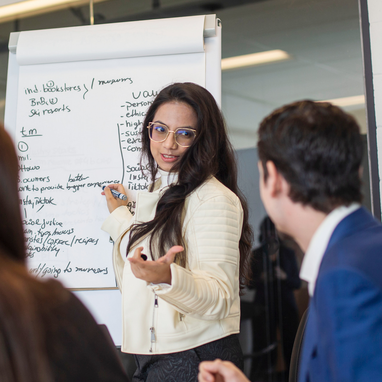 A woman standing in front of a group teaching, with notes on a board behind her