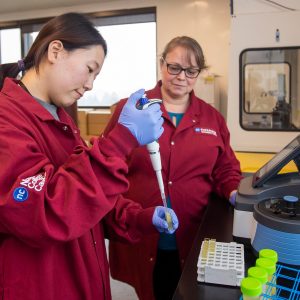 Two researchers in red lab coats, working in a lab