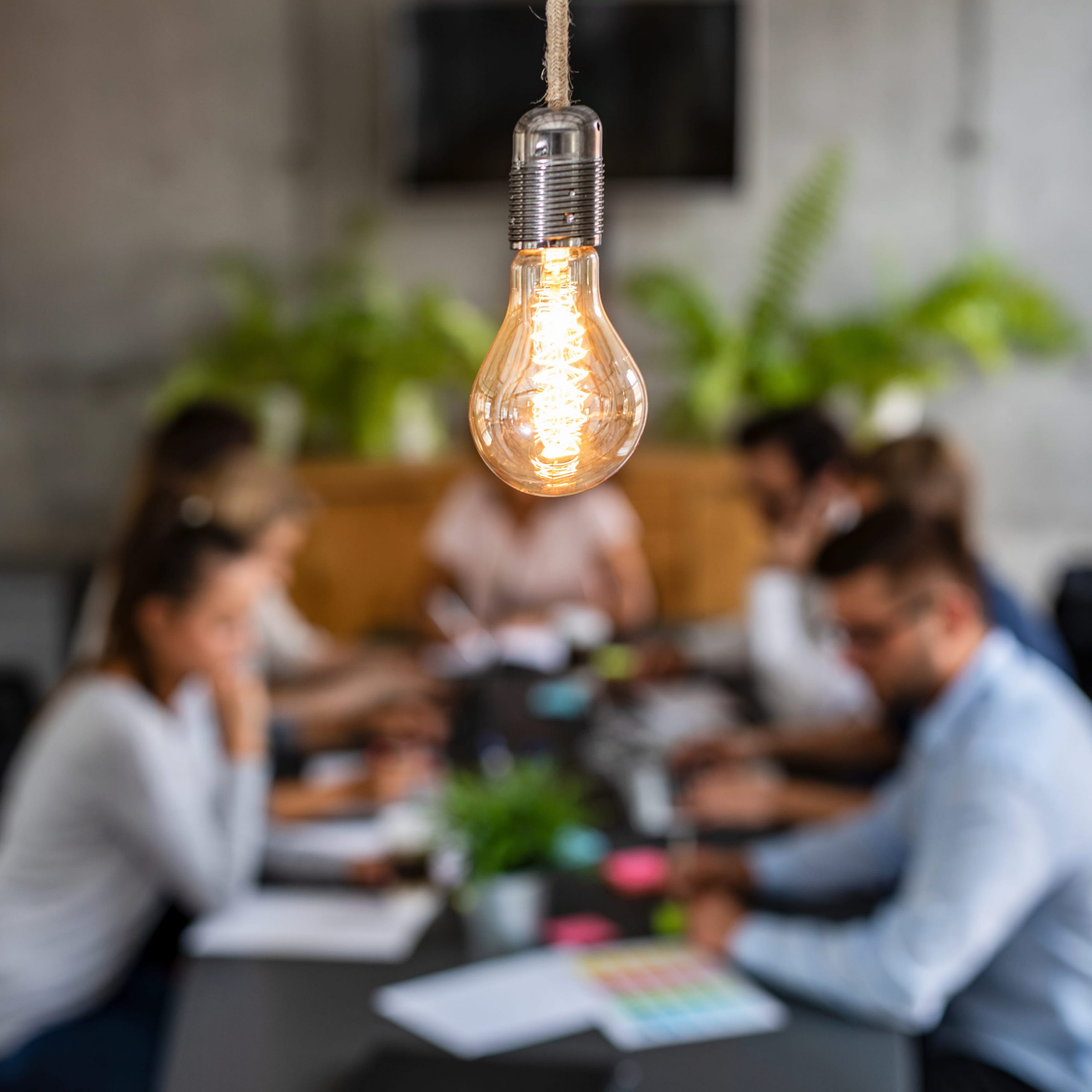 Focus on a bare lightbulb, with out of focus group of people sitting at a table together