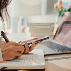 Close up of someone looking at a cell phone phone and taking notes in a notebook